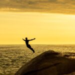 free-photo-of-man-jumping-to-sea-at-golden-hour